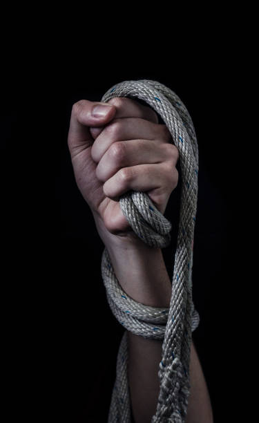 istockphoto-1081266282-612×612 Clenched fist and forearm on a black background entwined by a thick rope as a symbol of slavery and violence.